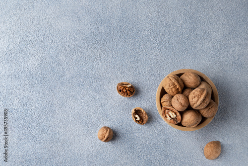 Top view of walnuts lying in a wooden bowl. Horizontal orientation, copy space, blue textured background.