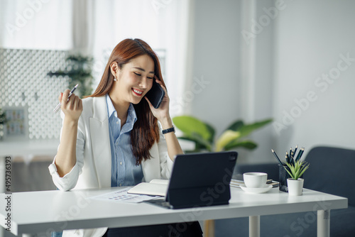 Confident Asian businesswoman documents working on laptop and talking on the phone at her workplace. reading financial reports analyzing statistics pointing at pie charts working at her desk.