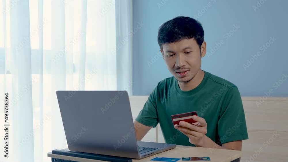 4K 50fps, Handsome Asian boy, wearing a green t-shirt, is shopping online through his laptop computer, and he is transferring money via credit card, a red card in his hand,shopping online. 4K 50fps, Handsome Asian boy, wearing a green t-shirt, is shopping online through his laptop computer, and he is transferring money via credit card, a red card in his hand,shopping online.