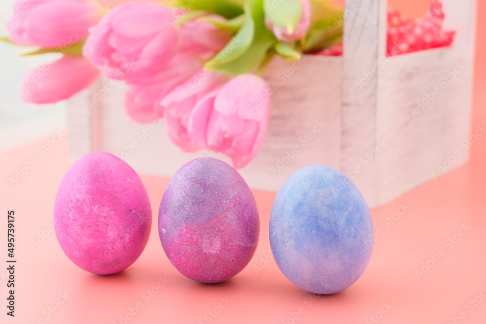 A beautiful delicate top bouquet of live spring pink tulips and pink, purple, blue eggs in a light wooden box on a pink background. Easter concept. Greeting card. A beautiful delicate top bouquet of live spring pink tulips and pink, purple, blue eggs in a light wooden box on a pink background. Easter concept. Greeting card.