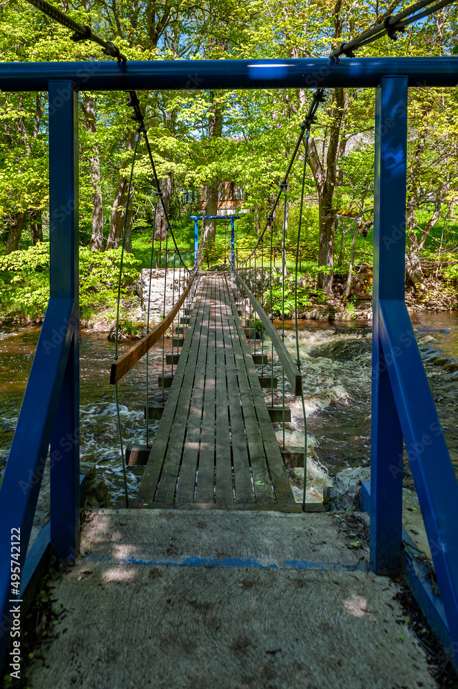 Suspension footbridge spans the river with waterfall. Joaveski waterfall. Estonia. Baltic. Suspension footbridge spans the river with waterfall. Joaveski waterfall. Estonia. Baltic.