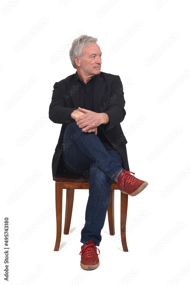 front view of a man sitting on chair with sneakers jeans and blazer, legs crossed and looking away on white background front view of a man sitting on chair with sneakers jeans and blazer, legs crossed and looking away on white background