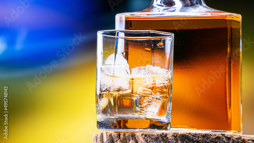 Cognac, whiskey in glass of ice stands next to bottle of full alcohol, amber color. Cold old whiskey in glass of ice is filled with half alcohol.