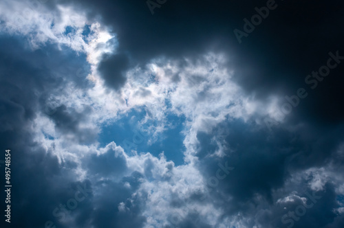 Rays of sun break through storm clouds against blue sky. Clouds on summer day against blue sky in sun's rays.