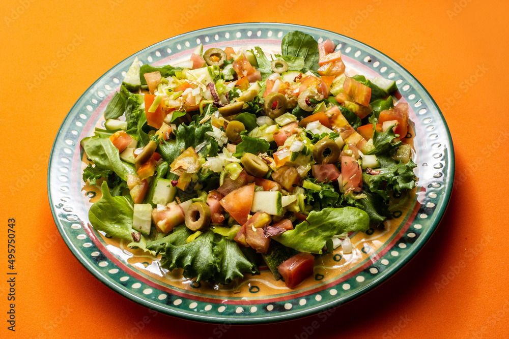 Um prato com salada de vegetais frescos sobre superfície de cor alaranjada. Um prato com salada de vegetais frescos sobre superfície de cor alaranjada.