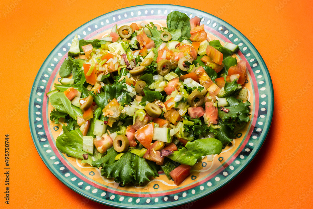Um prato com salada de vegetais frescos sobre superfície de cor alaranjada. Um prato com salada de vegetais frescos sobre superfície de cor alaranjada.