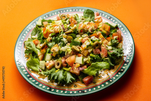 Um prato com salada de vegetais frescos sobre superfície de cor alaranjada.