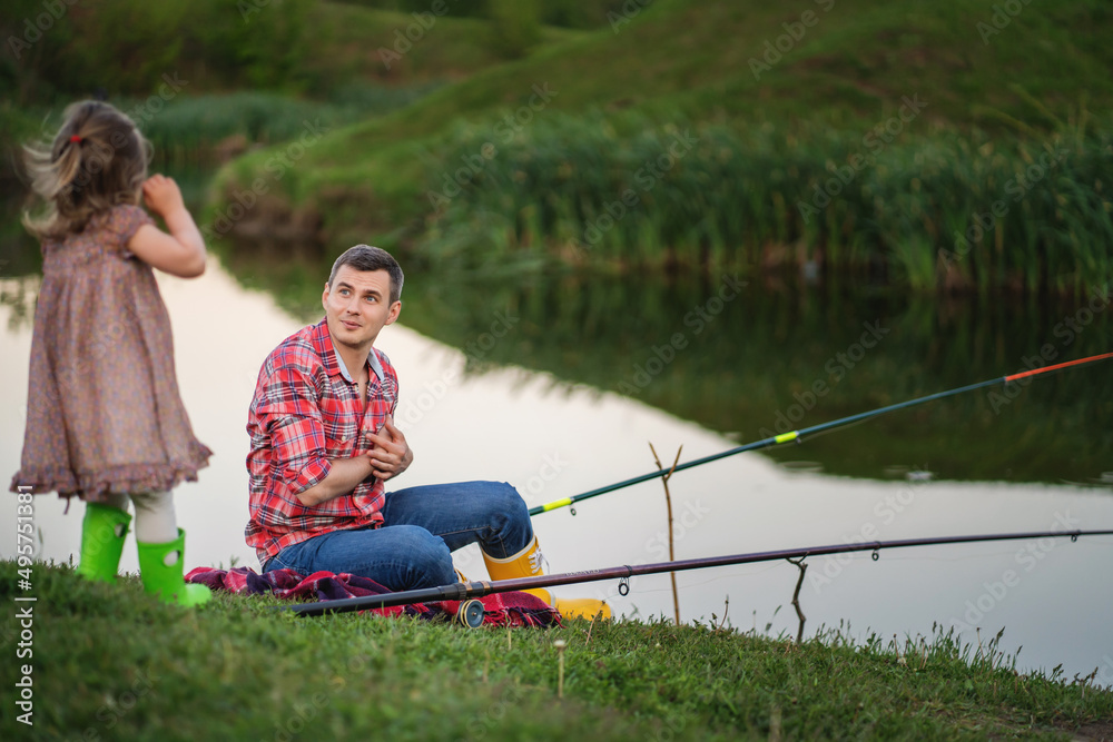 Dad is fishing on the lake. little daughter next to him runs and plays. single father concept Dad is fishing on the lake. little daughter next to him runs and plays. single father concept