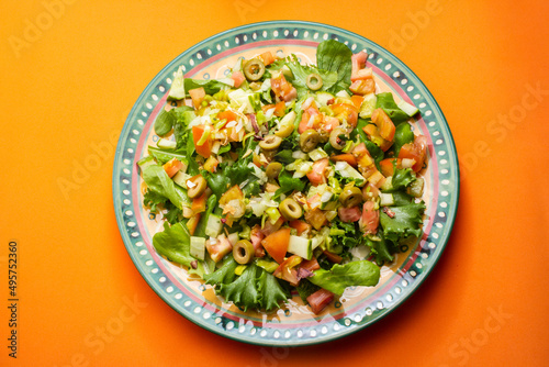 Um prato com salada de vegetais frescos sobre superfície de cor alaranjada.