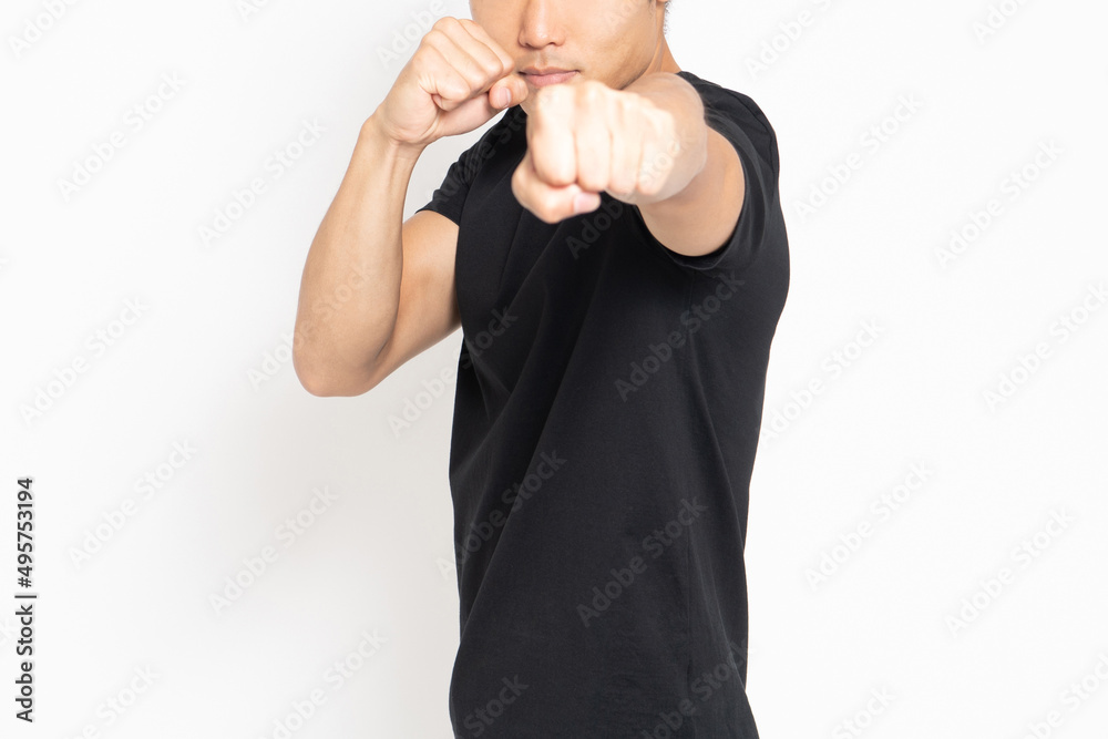 Fototapeta premium 白い背景の前に立ってパンチのポーズをする黒いTシャツを着ている男性