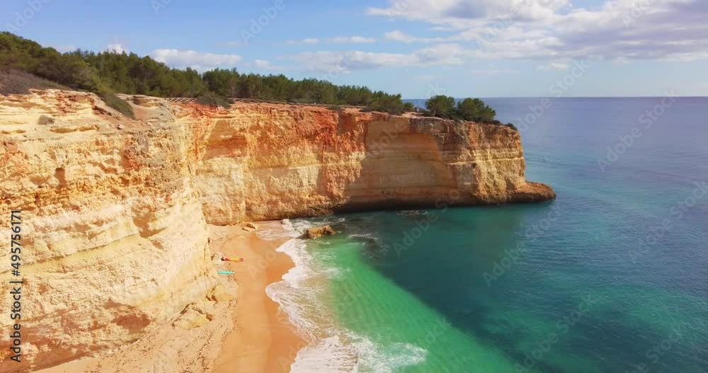 Waves slowly breaking on the empty beach on a hot summer day. No people, tropical beach. Golden cliffs and blue green water, sun reflecting. Water texture. Golden sands, limestones, rock formation Waves slowly breaking on the empty beach on a hot summer day. No people, tropical beach. Golden cliffs and blue green water, sun reflecting. Water texture. Golden sands, limestones, rock formation