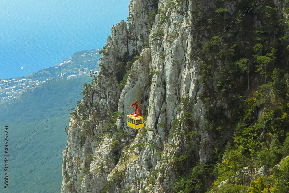 Yellow cabin of the funicular against the background of the steep Ai-Petri cliff in the Crimea. A view of the mountains, forest and sea from above. Cableway Miskhor-Sosnovy Bor-Ai-Petri Yellow cabin of the funicular against the background of the steep Ai-Petri cliff in the Crimea. A view of the mountains, forest and sea from above. Cableway Miskhor-Sosnovy Bor-Ai-Petri