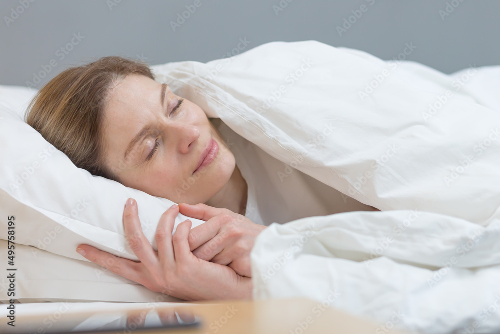 Close-up photo of a woman sleeping under a blanket smiling in a dream