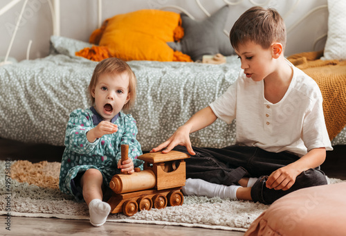 Cute teen boy and his little sister siting on fluffy rug on the floor of living-room and playing with wooden train after dinner photo
