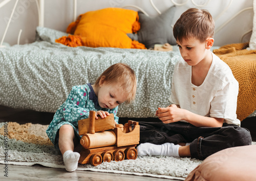 Cute teen boy and his little sister siting on fluffy rug on the floor of living-room and playing with wooden train after dinner photo