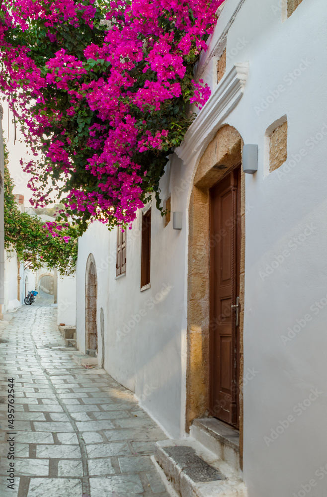 Narrow street in Lindos town on Rhodes island, Dodecanese, Greece. Beautiful picturesque old vintage white houses with flowers. Famous travel destination in Southern Europe