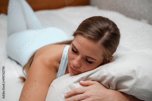 A young woman lies on a bed without a blanket. Bed linen is white.
