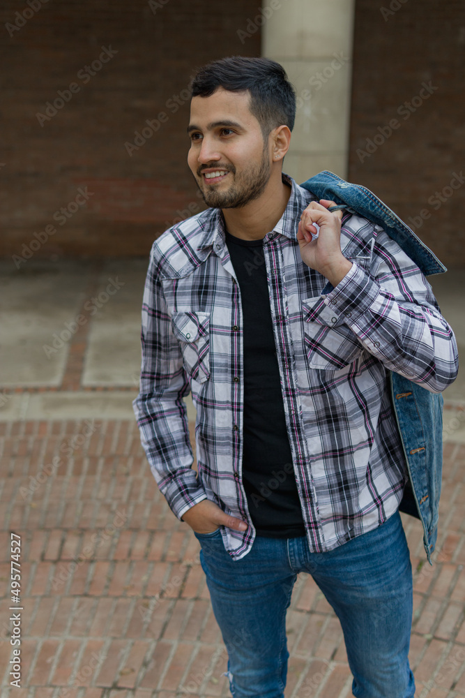 Obraz premium high angle shot of a nice-looking guy with hispanic features with one hand carrying his jacket over his shoulder and the other on his pocket while looking something smiling