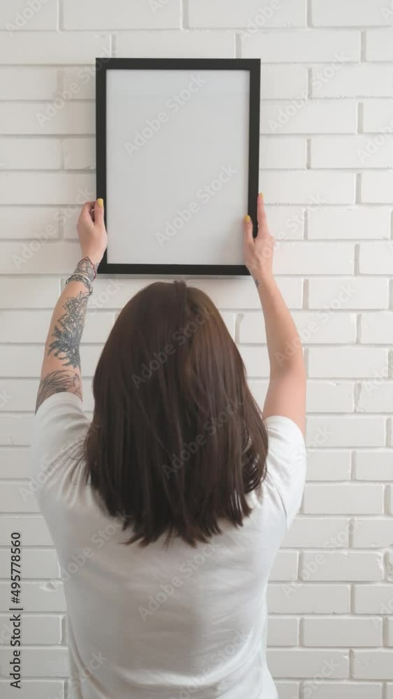 a girl hangs an empty frame on a white brick wall