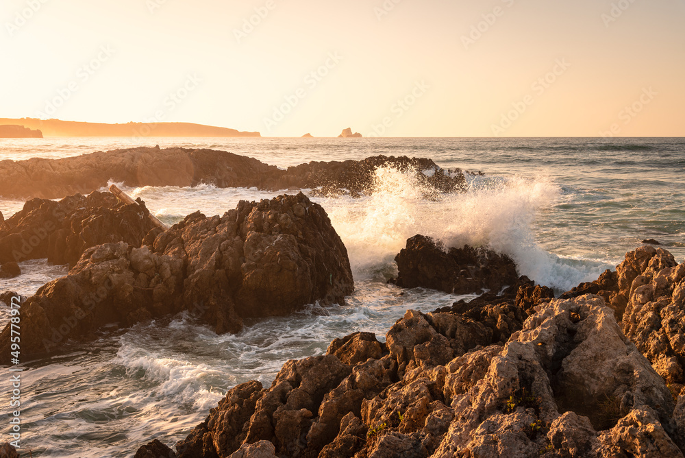 Rough sea waves hit the rocks at the famous surfing beach of Canallave at sunset, Dunas de Liencres Natural Park and Costa Quebrada, Cantabria, Spain Rough sea waves hit the rocks at the famous surfing beach of Canallave at sunset, Dunas de Liencres Natural Park and Costa Quebrada, Cantabria, Spain