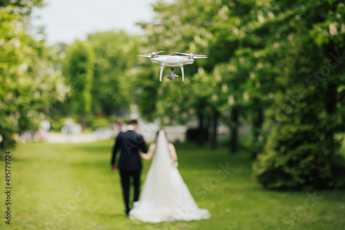 Obraz na płótnie Photo of a drone filming wedding couple while they walk along in the park at wedding day. w salonie