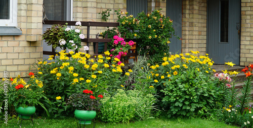 The porch of small house in rural style surrounded by perennial and annual colorful flowers  in summer.