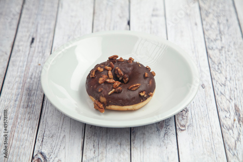 Chocolate donuts with hazel nuts on a white plate on Wood table 
