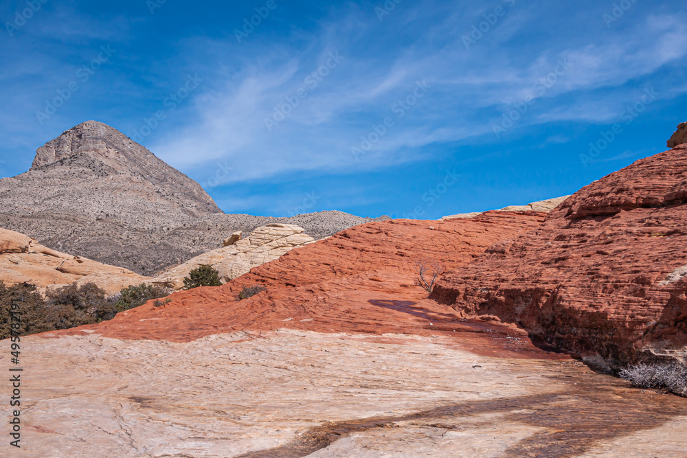 Las Vegas, Nevada, USA - February 23, 2010: Red Rock Canyon Conservation Area. Red rock dominates over beige with wet line under blue cloudscape. Gray mountain top on horizon.