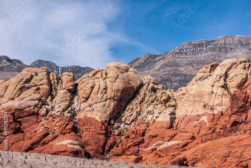 Las Vegas  Nevada  USA - February 23  2010  Red Rock Canyon Conservation Area. Beige rocky layer on top of red layer on mountains in front of snow capped gray mountain under blue cloudscape.