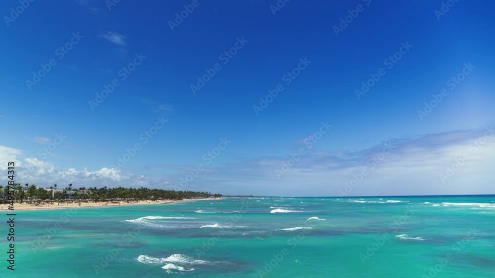 Seascape of tropical palm beach view from the sea. Turquoise ocean with white waves under a bright blue sky. Green peninsula on a sunny day. Journey to a tropical paradise. The beauty of the wild.