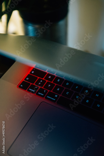 Vertical shot of a half-opened laptop keyboard with under the red light from the screen photo