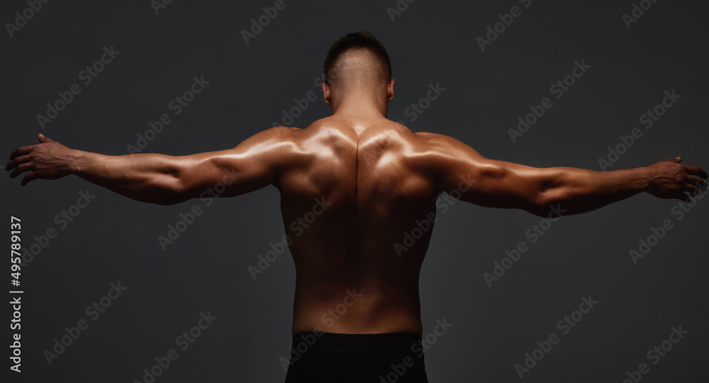 Back off. Rearview shot of an unrecognizable and athletic young man posing shirtless in studio against a dark background.