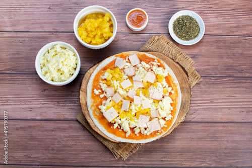 Artisan pizza before baking, with cheese, ham, pineapple, pomodoro sauce, accompanied by flavors