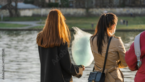 A girl holds cotton candy in her hand in the rays of evening backlight on the river bank