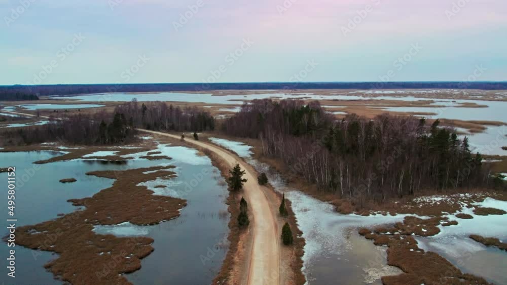 Camera flying from above the lake over the road, forest and field behind the lake, sunset. Aerial footage with the cinematic panoramic camera motion Camera flying from above the lake over the road, forest and field behind the lake, sunset. Aerial footage with the cinematic panoramic camera motion