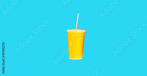 Close up of yellow cup of juice with straw on blue background, top view
