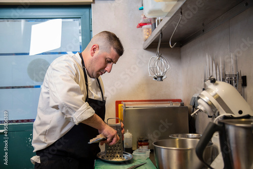 chef usa rallador metalico para queso parmesano en interior cocina de restaurante con uniforme blanco y mandil negro 
