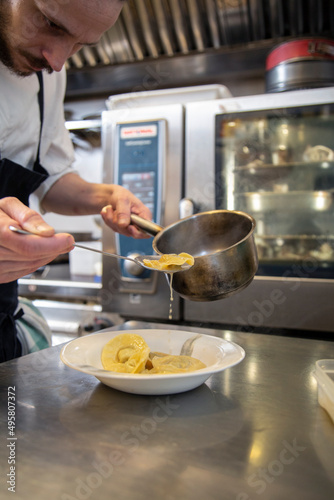 chef manos cocina  fresca tortellini con salsa sirve en plato blanco en interior cocina restaurante con uniforme blanco y mandil negro close-up