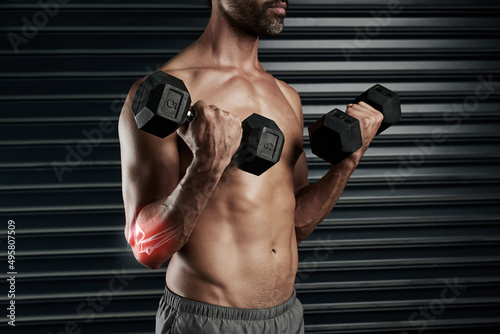 Pushing himself a little too far. Studio shot of a muscular young man lifting dumbbells with cgi highlighting his elbow.