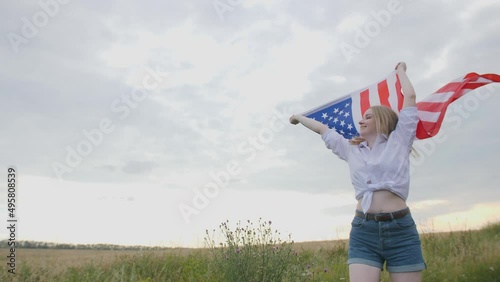 Patriotic young woman holds the US flag and runs across the field