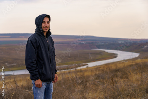 smiling man hiker in a windbreaker at dawn in a good mood. Portrait on a blurred background of nature and water photo