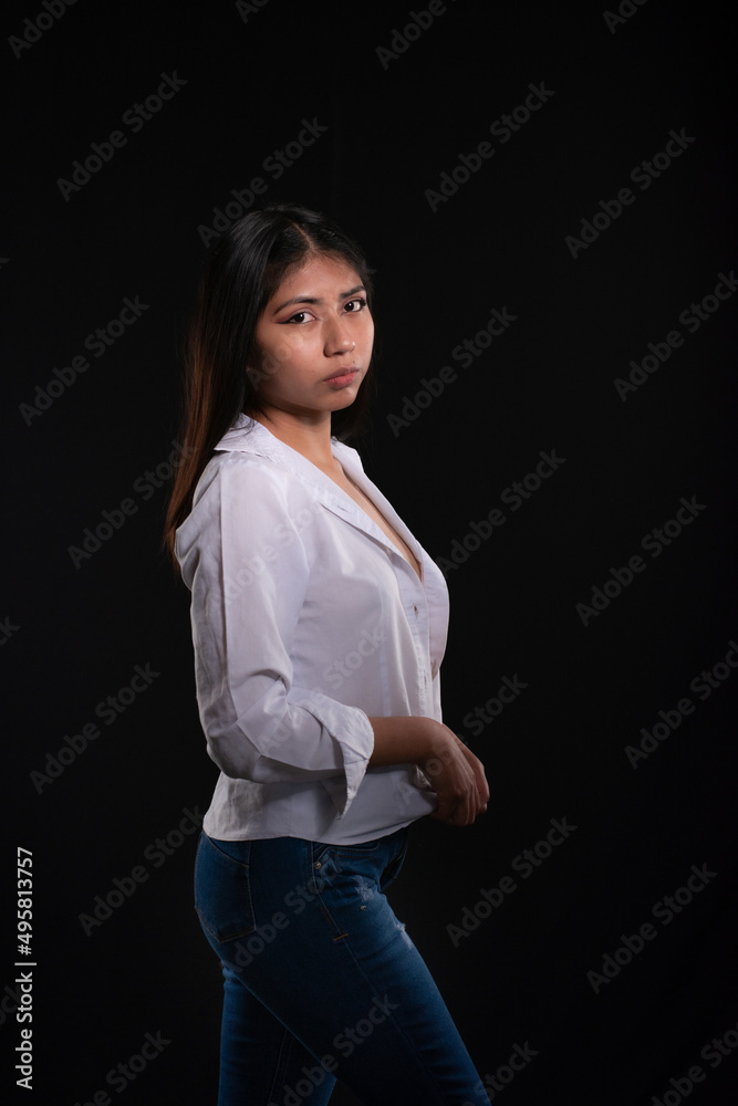 frontal portrait of Hispanic girl in studio isolated on black background with white shirt, alternative modeling concept.