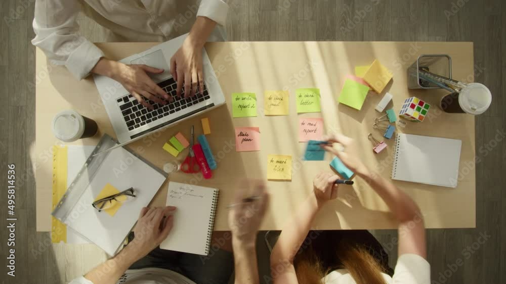 Business people working in modern office together top view. Creative workers discussing tasks, writing notes on colourful stickers. Project planning, group brainstorming. Team leader typing on laptop.