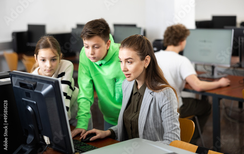 Friendly female teacher and positive teen students looking at monitor screen during lesson in computer lab at school library .. © JackF