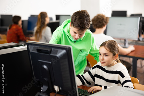 Smart interested preteen schoolboy helping cute girl classmate sitting at computer during informatics lesson..
