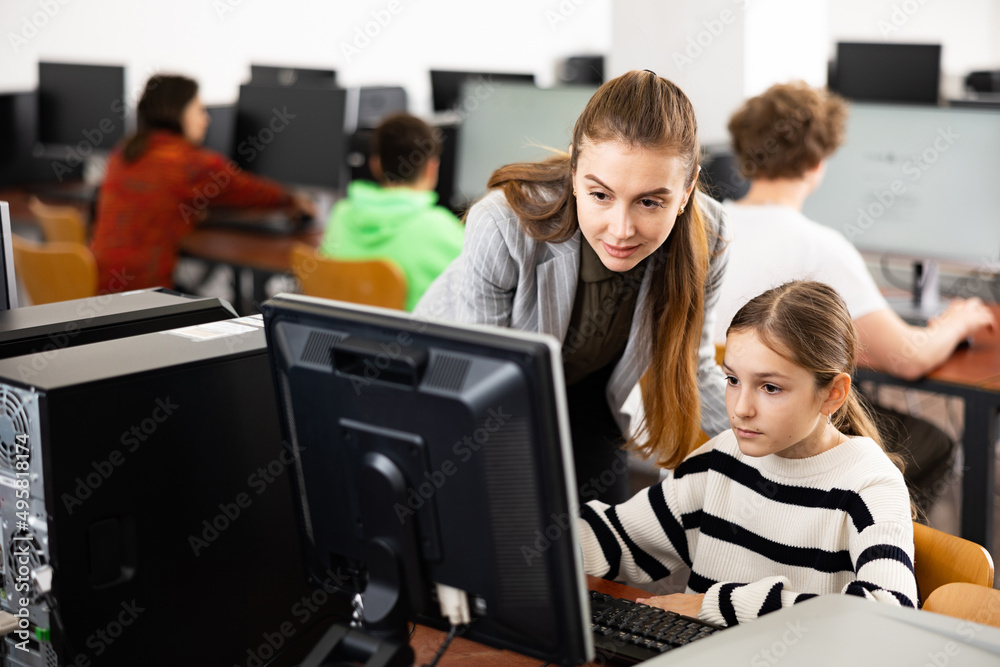 Fototapeta premium Teacher helping young girl to solve computer problem during lesson.