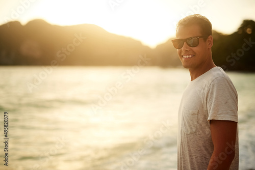 No better place than the beach. Portrait of a handsome young man standing on the beach at sunset.