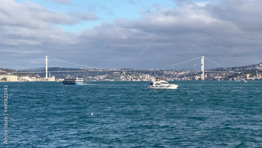 Istanbul, Turkey - January 2022: Passenger boat and a yacht in bosphorus sailing with 15 July Martyrs Bridge in background Istanbul, Turkey - January 2022: Passenger boat and a yacht in bosphorus sailing with 15 July Martyrs Bridge in background