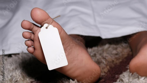 The dead man's body with blank tag on feet under white cloth in a morgue photo