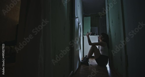 Woman smoking weed in corridor. Zoom in view of female junkie igniting and smoking marijuana joint while sitting on floor in dark hallway at home